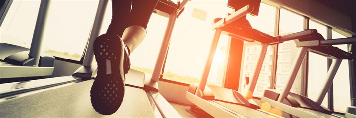 Person running on a treadmill in a gym with sun coming through the windows