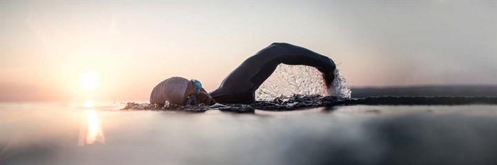 Man swimming outside with sunrise in background
