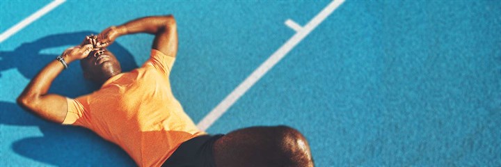 Man lying on his back on a blue athletic race track