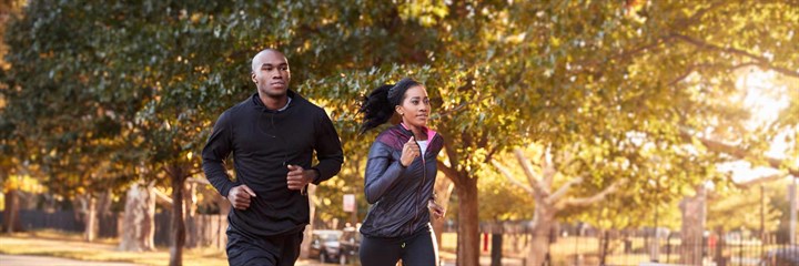 Man and woman jogging in the park with trees and sun shining in background