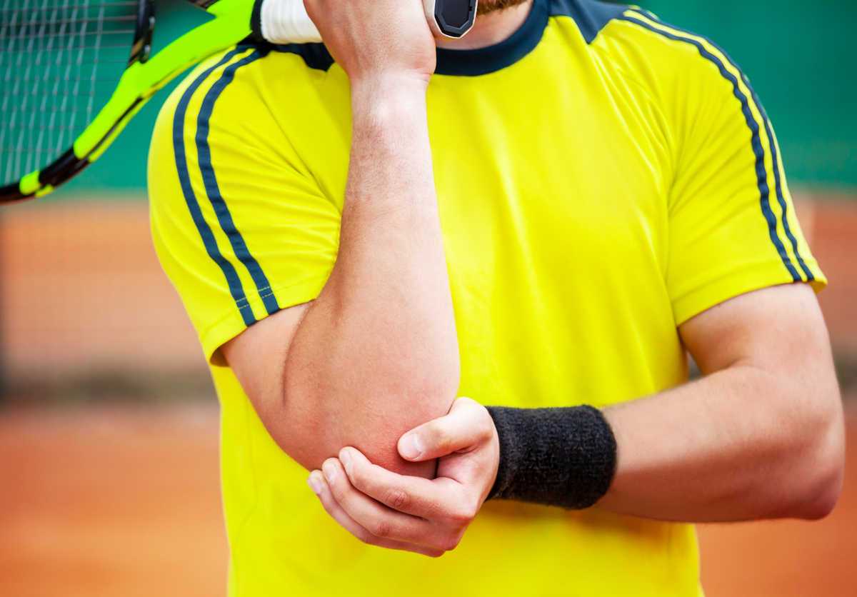 Man clutching elbow, holding tennis rackket