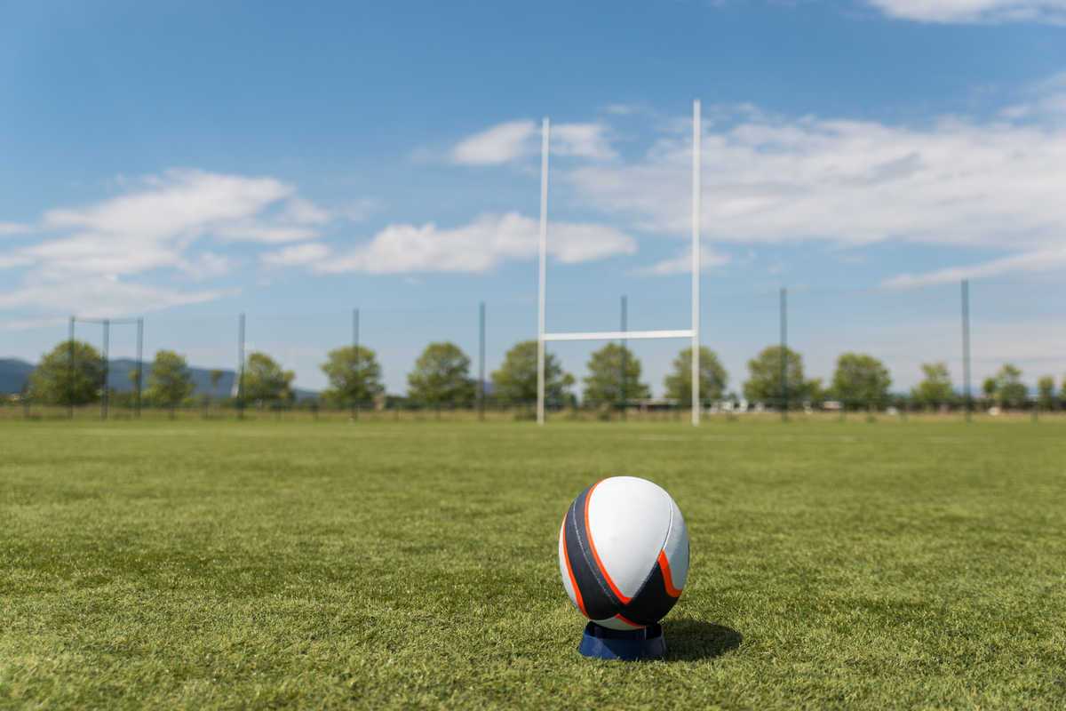 Rugby ball on empty field with rugby goal posts in distance
