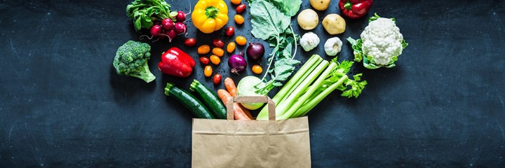 Brown paper bag with lots of vegetables coming out of the top 