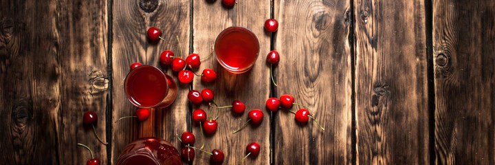 Overhead shot of cherry juice and cherries on a wooden background